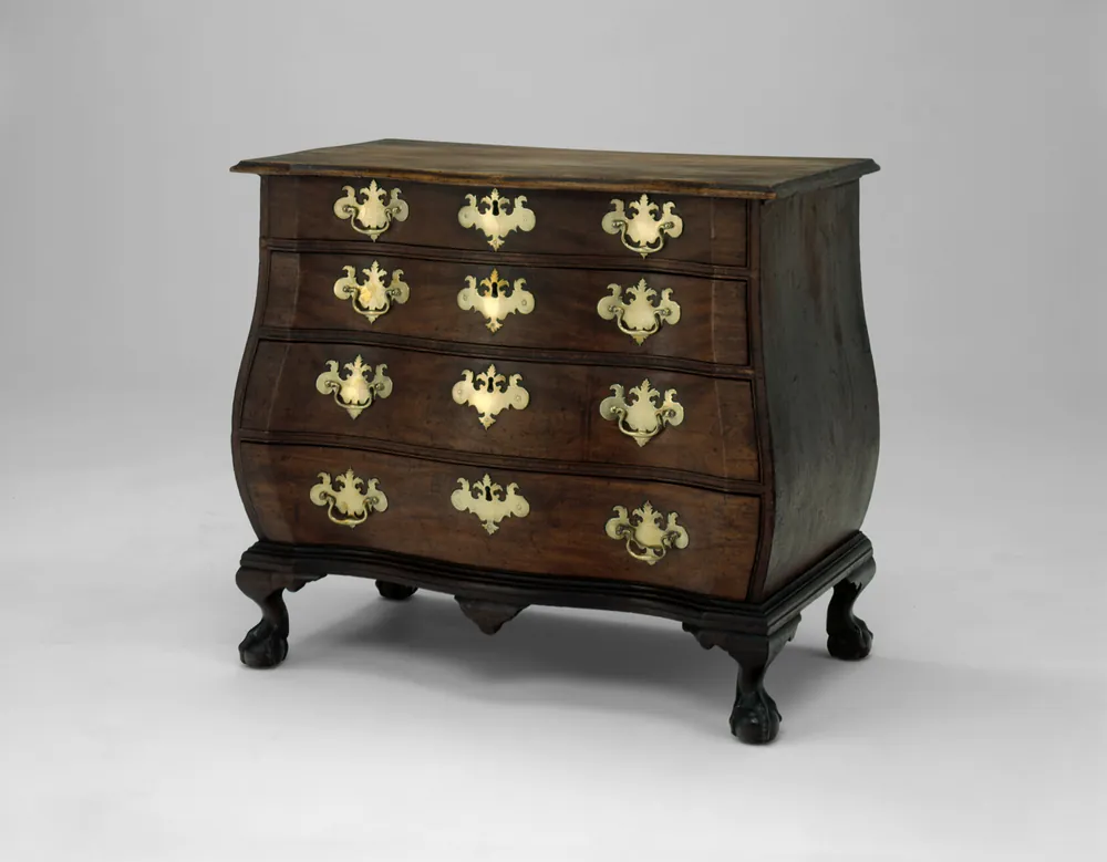 A bombé chest of drawers in dark mahogany with shaped sides, four graduated drawers, pierced brass handles and carved ball-and-claw feet