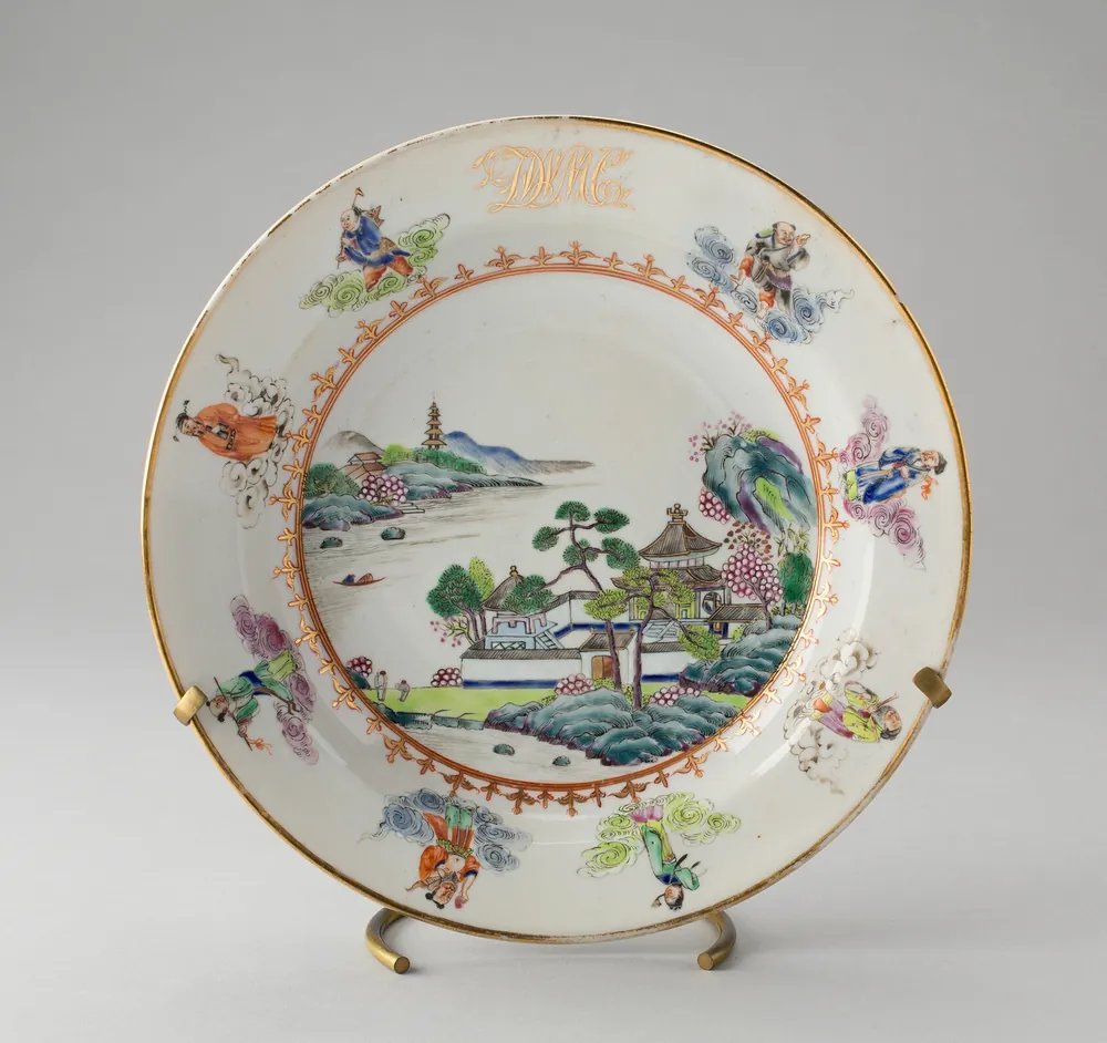 A Chinese export porcelain dinner plate painted with a river landscape, figures on clouds around the rim, and a gilt monogram at the top